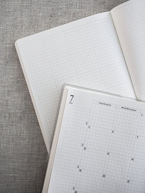 Minimalistic white planner spread featuring structured monthly pages with printed date grids and clear headings for organizing weekly schedules.