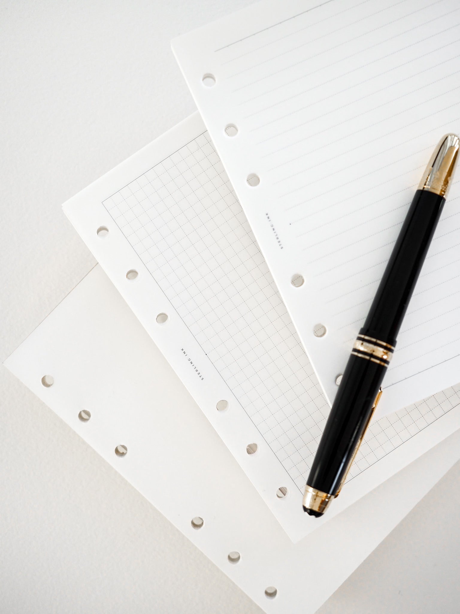Stacked sheets of white graph paper featuring precise 3.7mm grid lines and reinforced holes for binding, displayed with a sleek black pen.