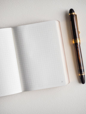 Open notebook showing clean, light gray grid lines across the pages and visible page numbering for detailed and organized note-taking.
