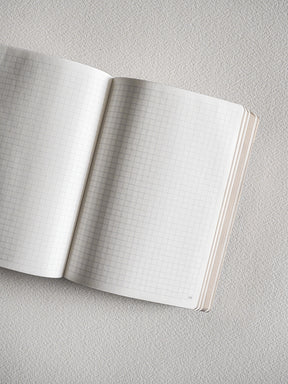 Open A6 grid notebook showing pristine white pages with a faint graph paper grid, ideal for organized journaling, study, or detailed note-taking.