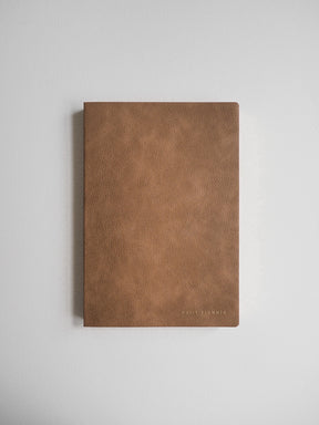 Minimalist A5 undated daily planner featuring a solid, matte camel brown faux leather cover and subtle branded detail.