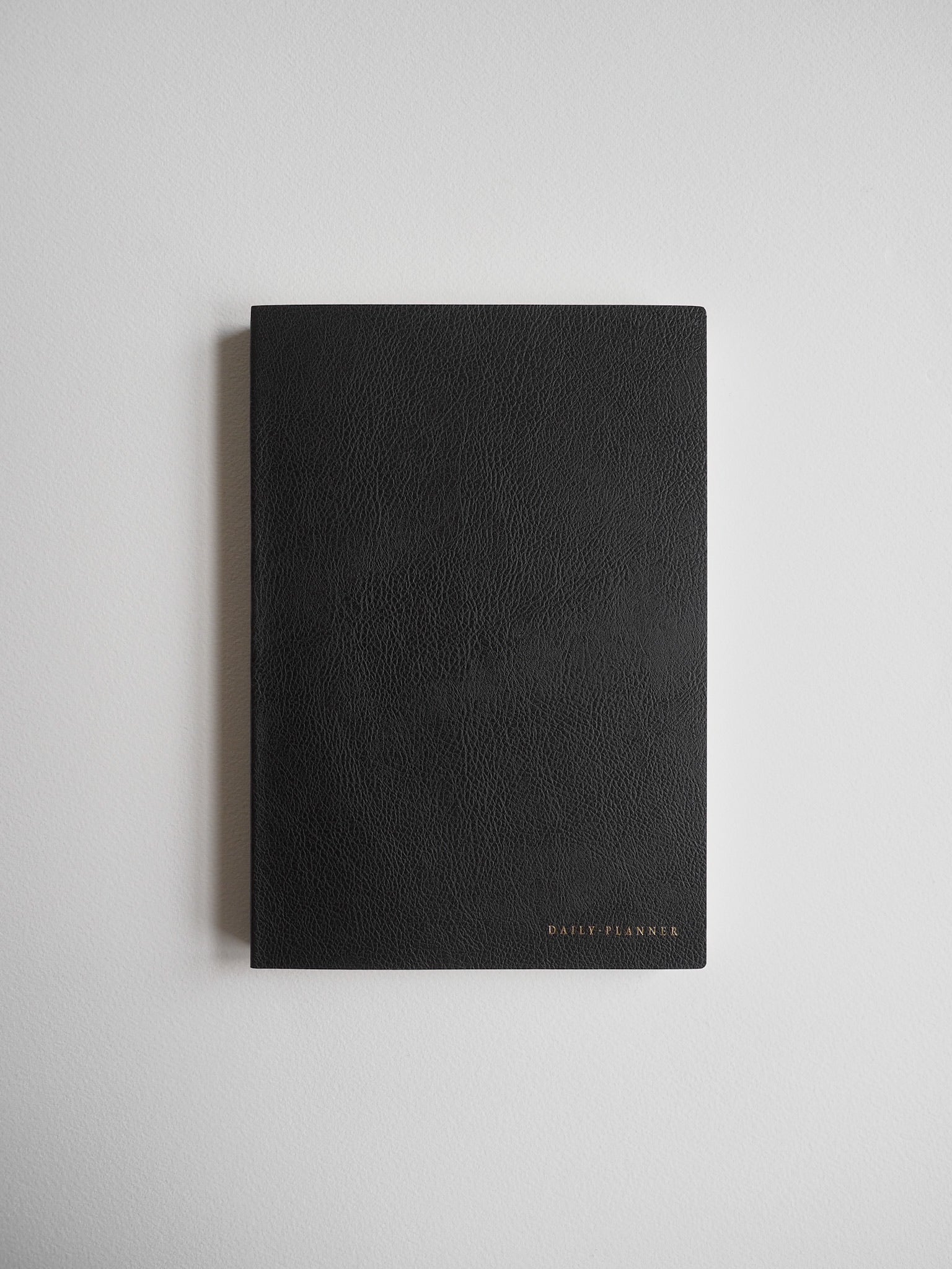 Matte black A5 daily planner with clean lines and a refined, minimal aesthetic, featuring delicate gold foil lettering on the solid cover.
