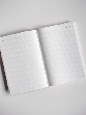 An open A5 undated planner showcasing light-grid graph paper pages perfect for daily journaling, note-taking, and scheduling.