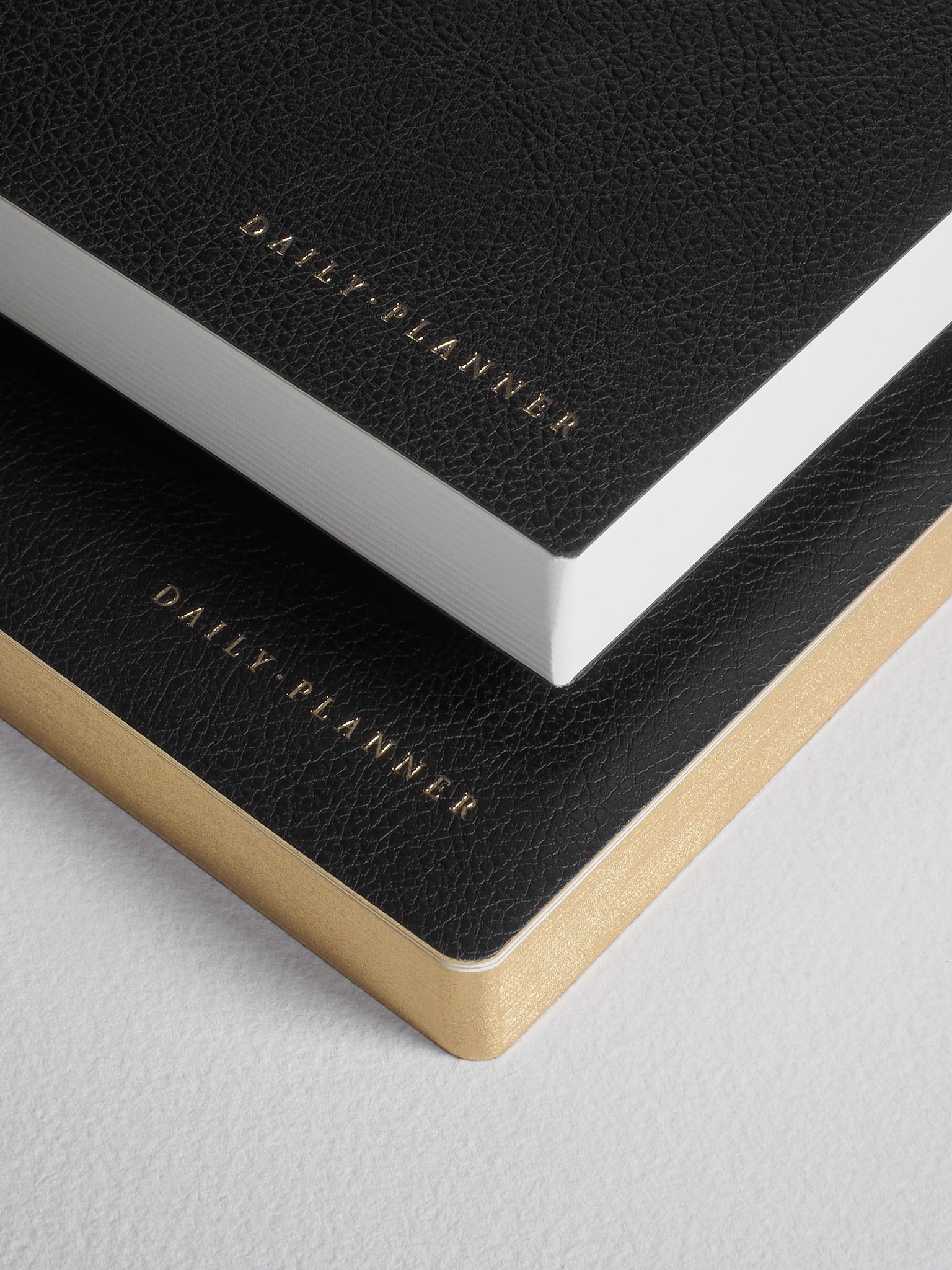 Stack of elegant A5 undated planners featuring deep black textured covers and detailed metallic gold "DAILY PLANNER" embossing.