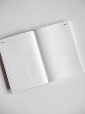 Open, undated B6 daily planner featuring white grid paper, perfect for graph note-taking, bullet journaling, and year-long organization.