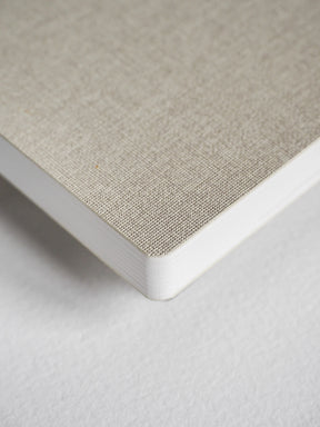 Close-up of a notebook corner showing a light beige linen-textured cover and white page edges on a white background.
#Color_Linen