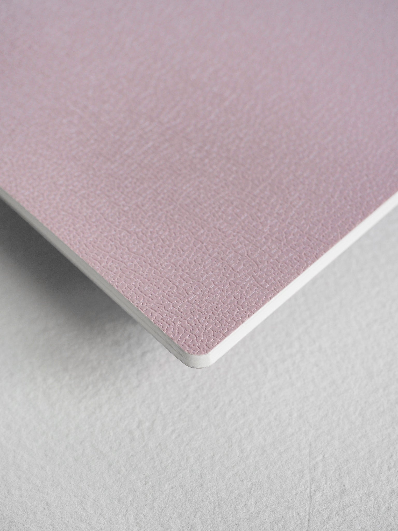 A compact passport notebook featuring a soft, pale dusty rose cover with a subtle, sophisticated textured finish, ideal for writing and journaling.