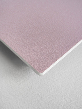 A compact passport notebook featuring a soft, pale dusty rose cover with a subtle, sophisticated textured finish, ideal for writing and journaling.