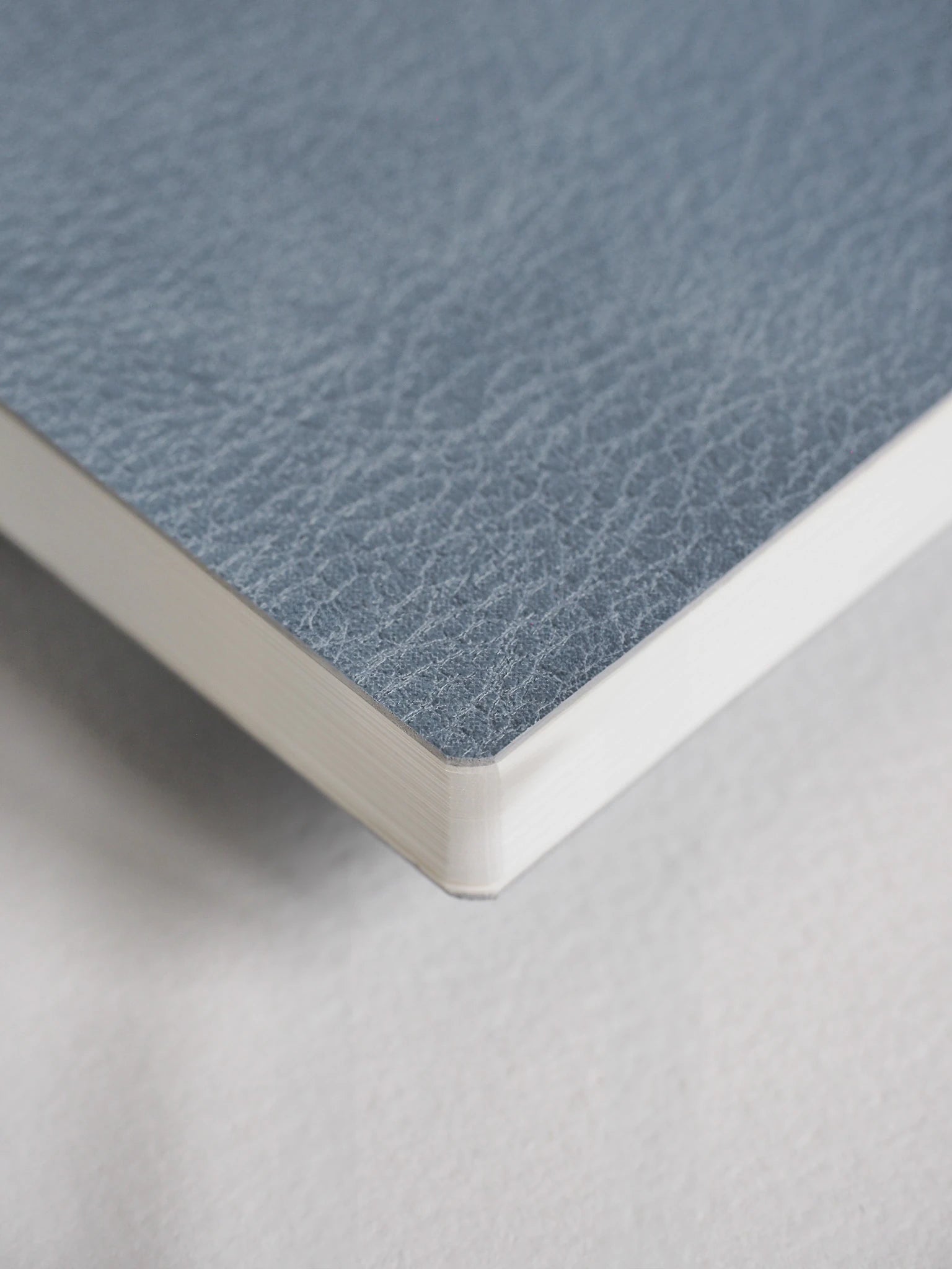 A close-up of a notebook or book corner showing a textured blue-gray cover and white page edges on a light neutral background.
#Color_Mist