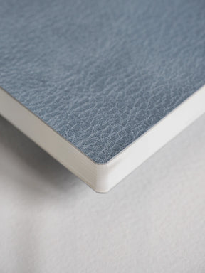 A close-up of a notebook or book corner showing a textured blue-gray cover and white page edges on a light neutral background.
#Color_Mist