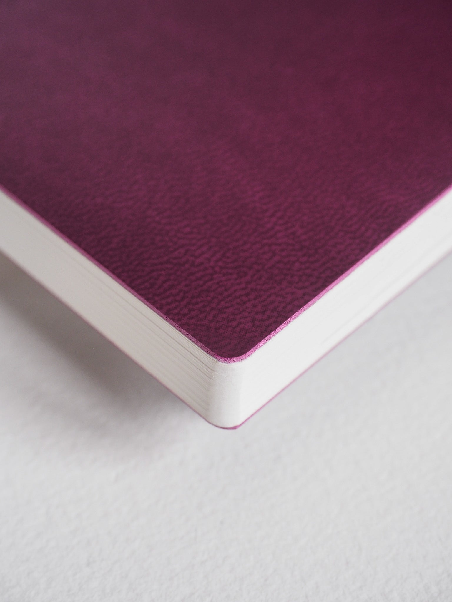 A closed notebook featuring a richly textured, deep plum-colored cover and visible stacked edges of crisp white paper.