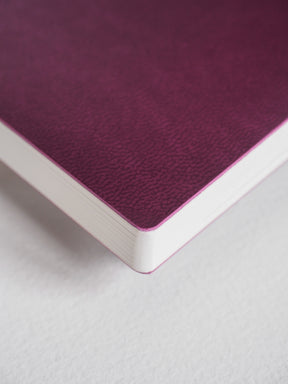 Rich plum-colored notebook featuring a finely textured cover and exposed crisp white interior pages for detailed writing and planning.