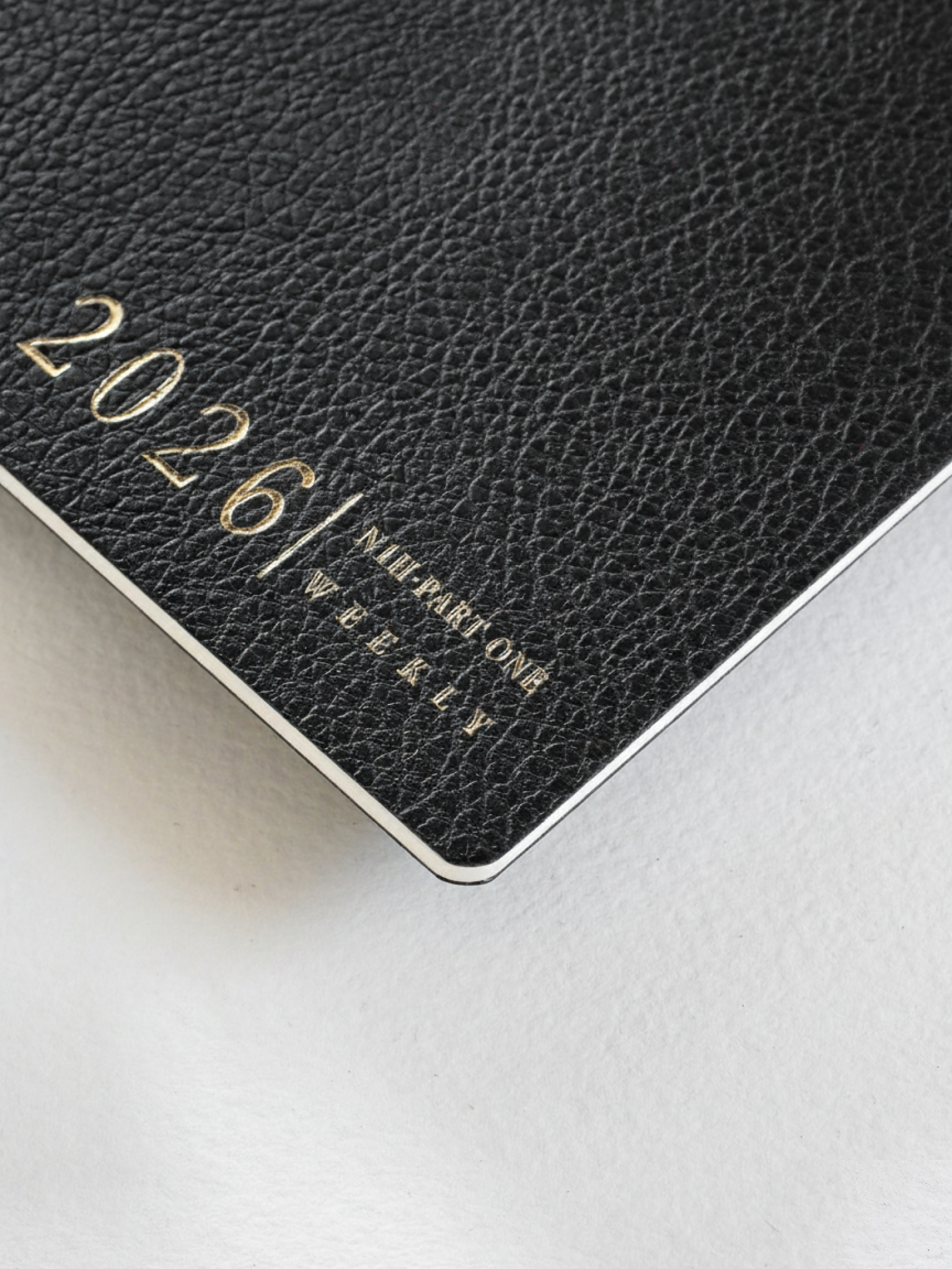 Dark, textured black weekly planner booklet featuring embossed gold lettering displaying "2026/ N1 PART ONE WEEKLY."