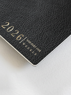 Dark, textured black weekly planner booklet featuring embossed gold lettering displaying "2026/ N1 PART ONE WEEKLY."