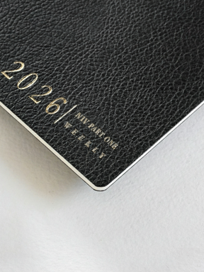 Luxurious black textured weekly booklet cover accented with shimmering gold foil lettering proclaiming "2026" and "N1 Vertical Weekly."