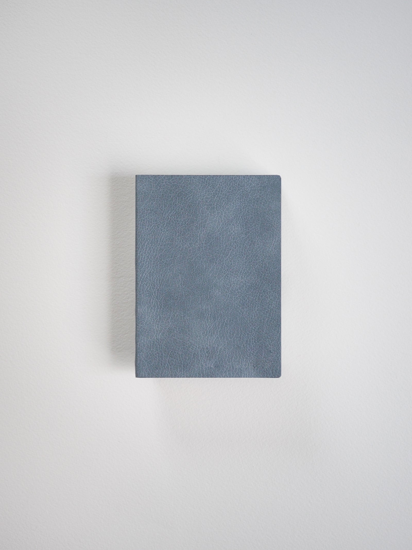 A rectangular notebook featuring a smooth, muted slate blue, matte faux leather cover.