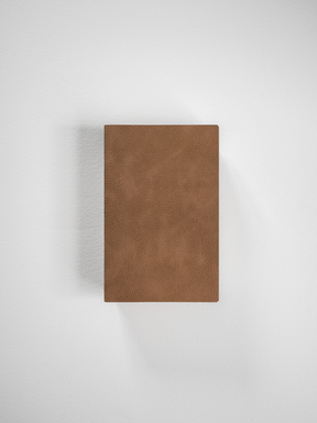 Portable grid notebook bound with a solid, medium brown faux leather cover, designed for everyday writing and planning.