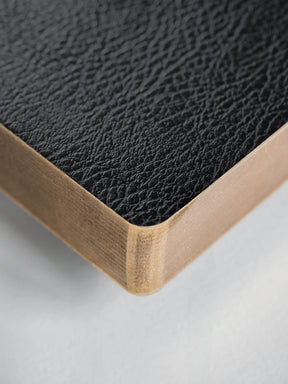 Close-up of a black textured leather or faux-leather surface with a light natural wood edge, shown on a plain light background.
#Color_Onyx
