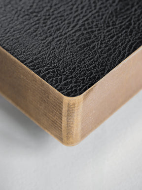 Close-up of a corner showing a black textured leather top surface and a light natural wood side edge on a white background.
#Color_Onyx
