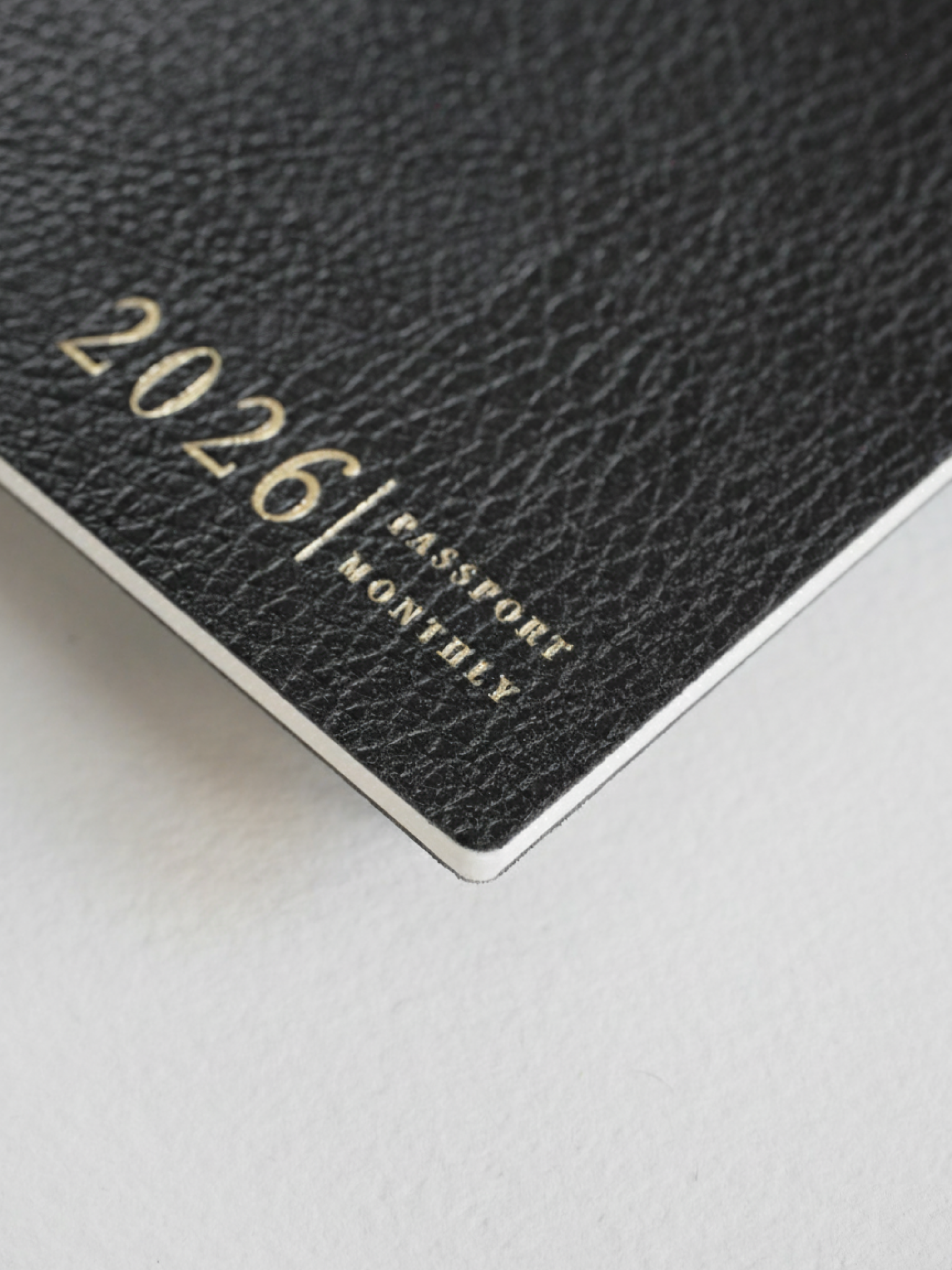 Dark, textured planner booklet featuring elegant gold foil lettering that reads "2026 | PASSPORT MONTHLY," perfect for organized annual planning.