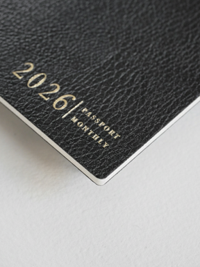 Dark, textured planner booklet featuring elegant gold foil lettering that reads "2026 | PASSPORT MONTHLY," perfect for organized annual planning.