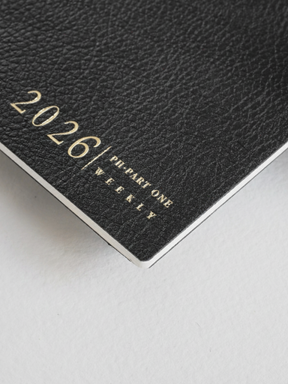 Dark black weekly planner booklet featuring the metallic lettering "2026 | PH-PART ONE WEEKLY" printed on the textured cover.
