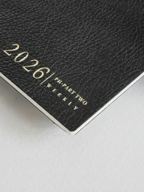 Black weekly planner booklet featuring a sophisticated, textured cover and prominent white text displaying "2026 | PI-PART TWO | WEEKLY."