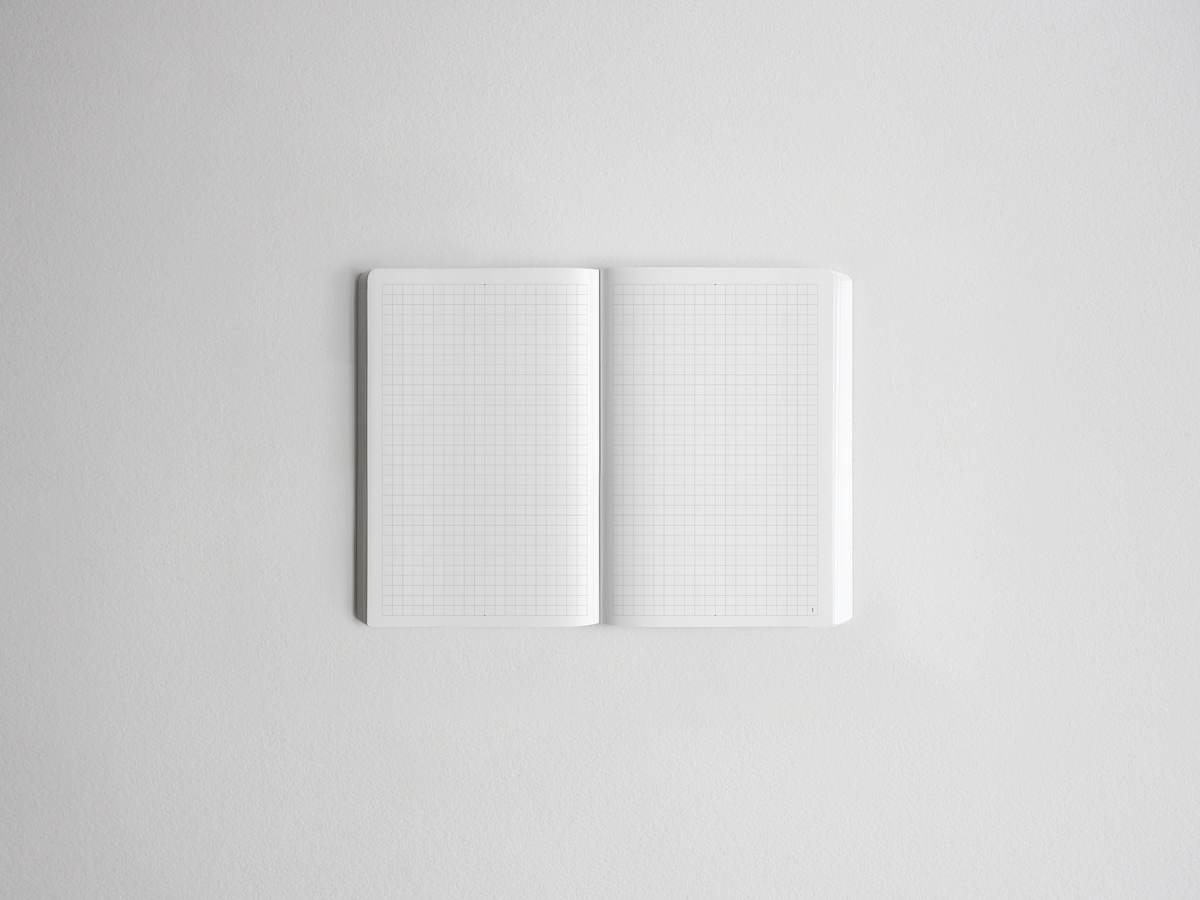 An open notebook with white grid paper pages, photographed from above on a clean, light gray background.