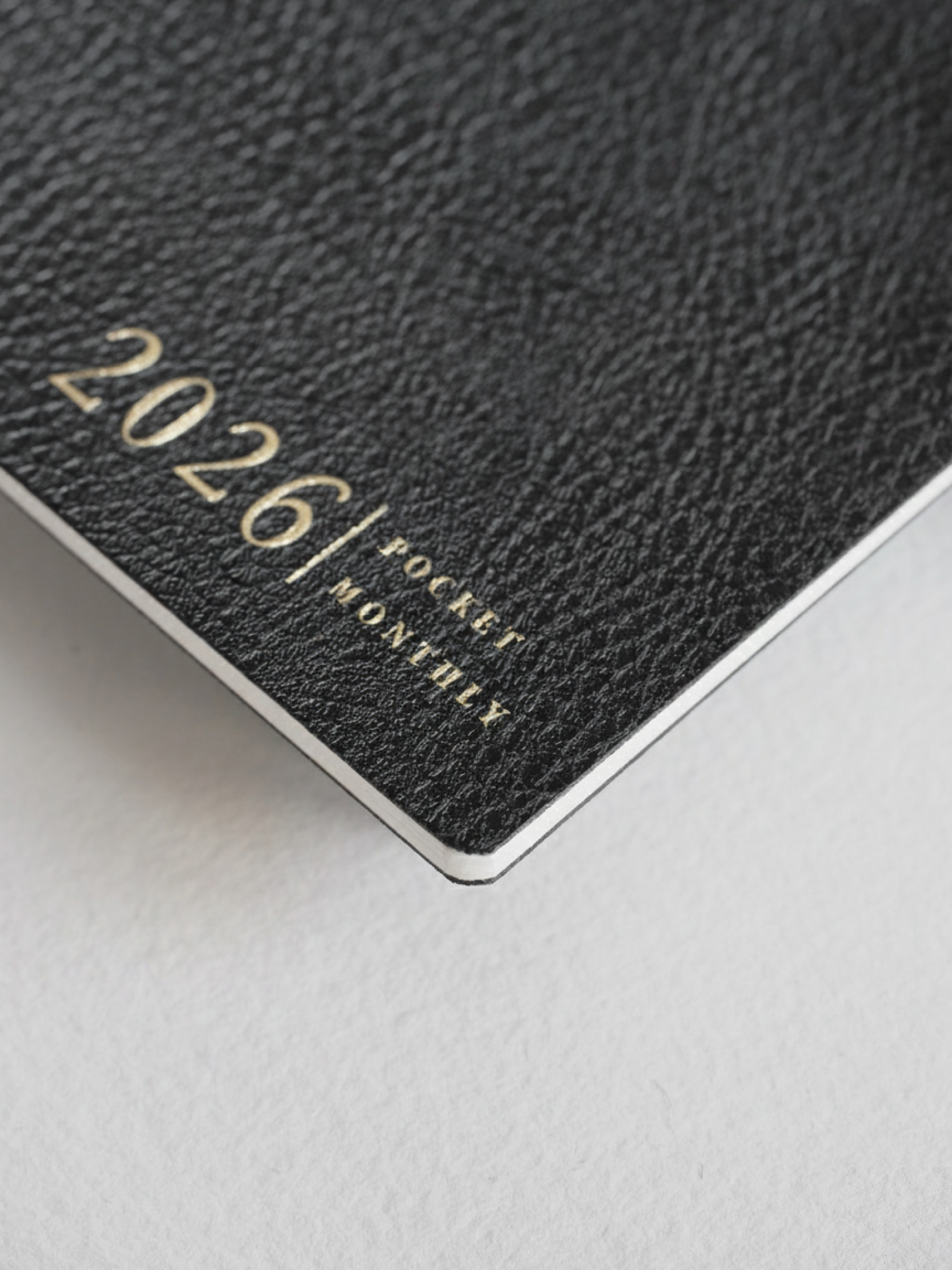 Deep black, textured pocket booklet cover featuring elegant gold lettering that reads "2026/ POCKET MONTHLY," perfect for planning.