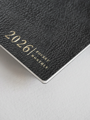 Deep black, textured pocket booklet cover featuring elegant gold lettering that reads "2026/ POCKET MONTHLY," perfect for planning.