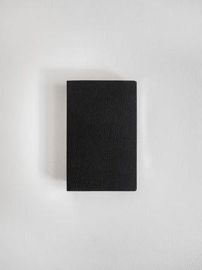 Minimalist pocket notebook featuring a deep black, smooth matte cover, perfect for versatile writing and on-the-go journaling.