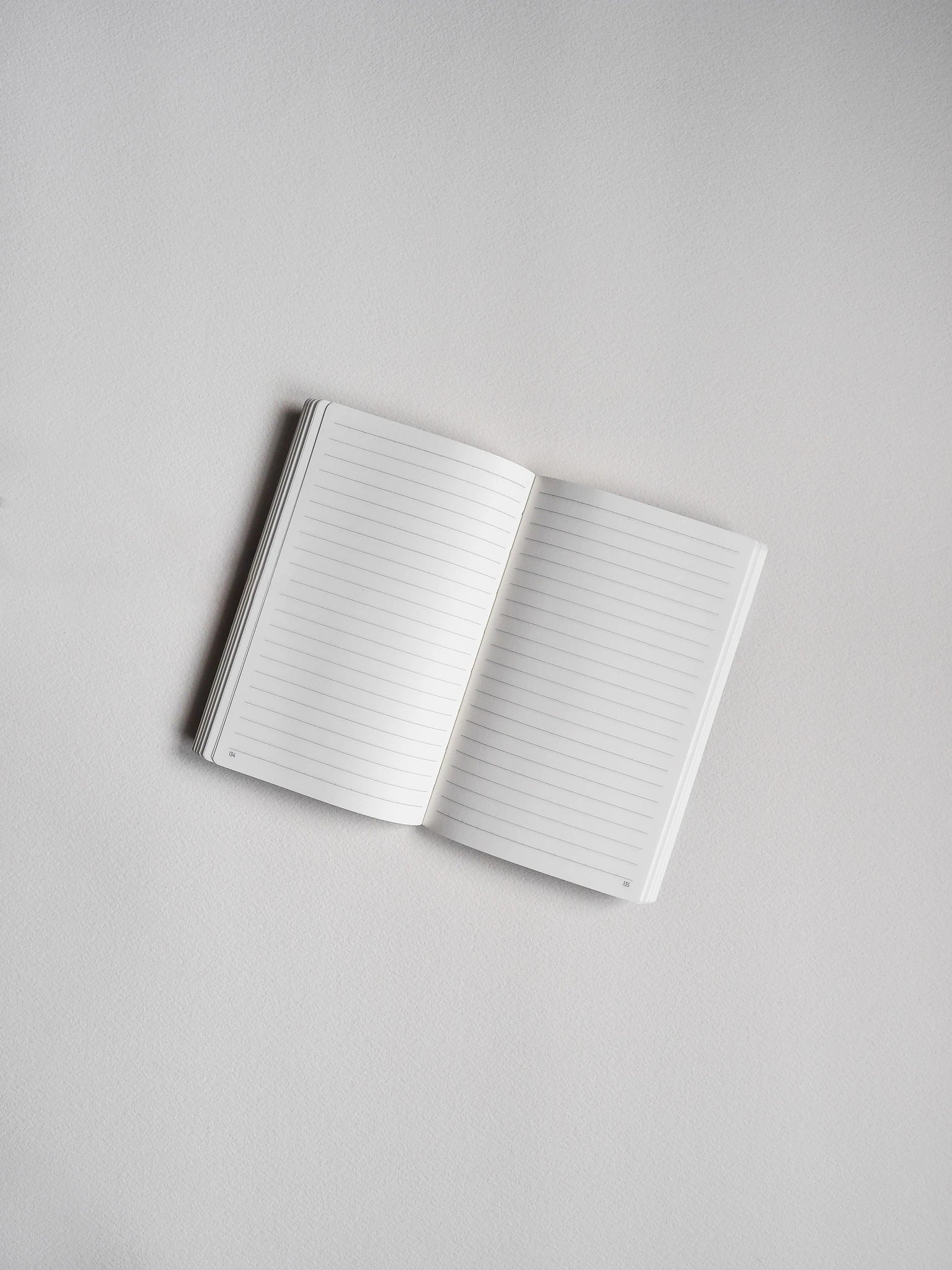 An open lined notebook with blank white pages, photographed from above on a light gray background.