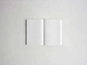 An open white grid notebook or planner with two blank pages, photographed from above on a light gray background.