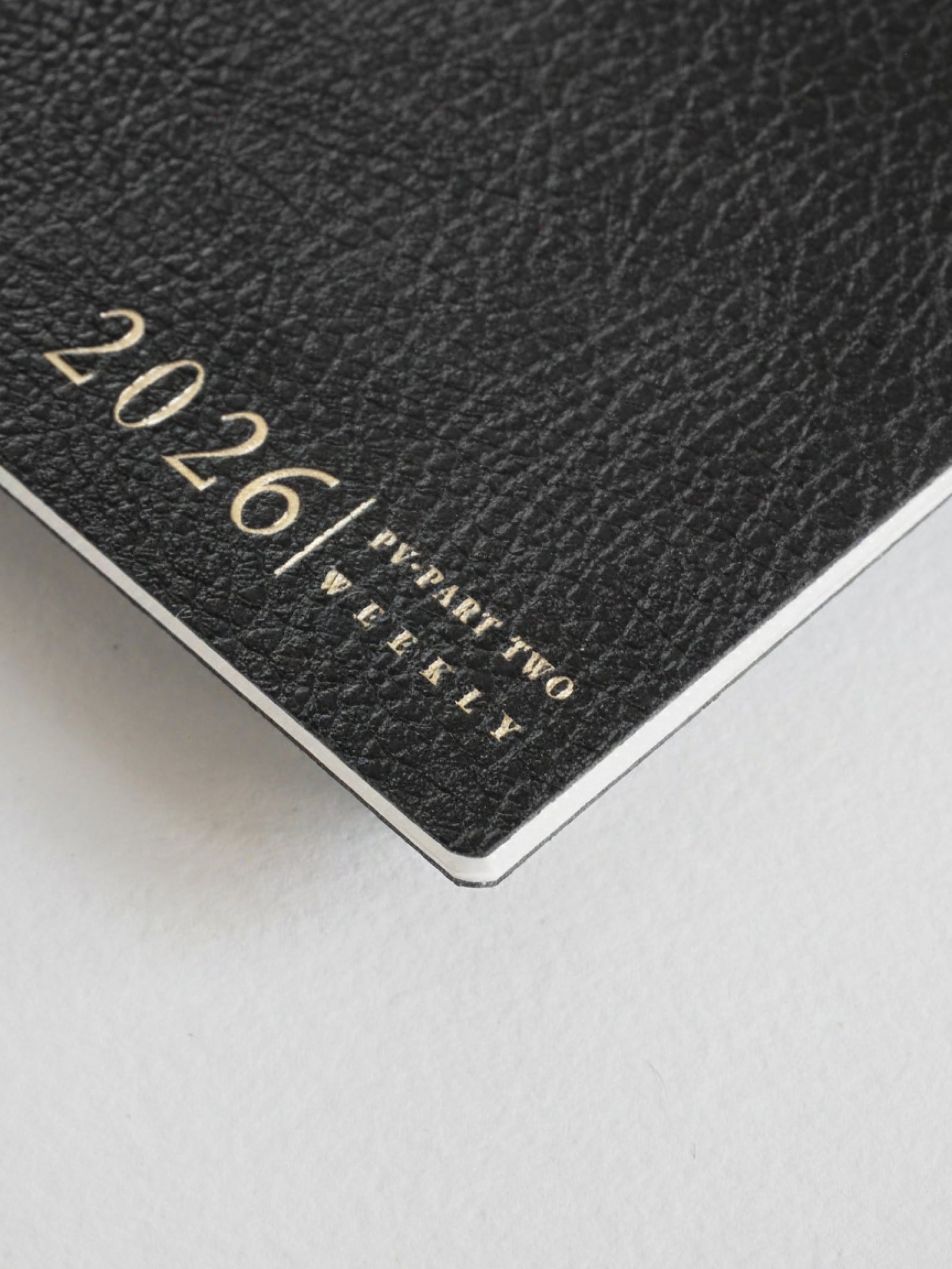 Black, textured passport-style weekly planner booklet featuring embossed text that reads "2026/ PV-PART TWO WEEKLY" for year planning.