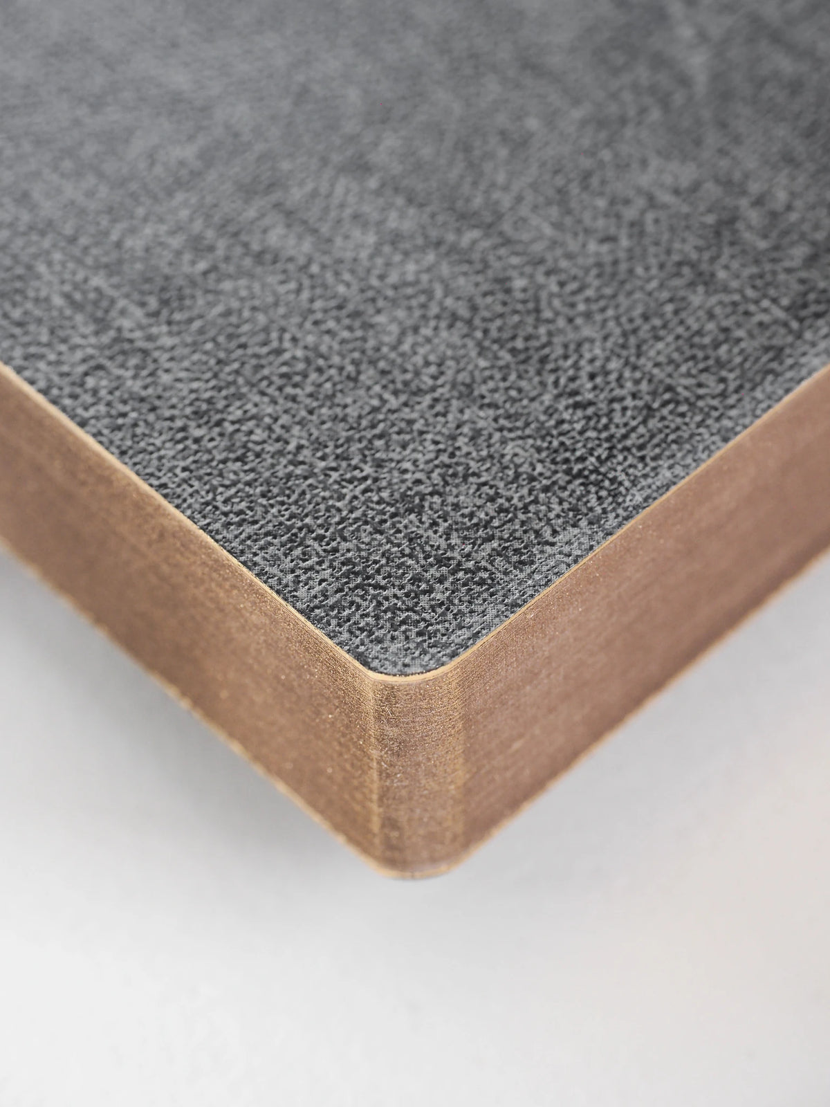 A close-up of a notebook or book corner showing a textured gray cover and white page edges on a light neutral background.
#Color_Tweed