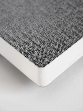 A close-up of a notebook or book corner showing a textured gray cover and white page edges on a light neutral background.
#Color_Tweed