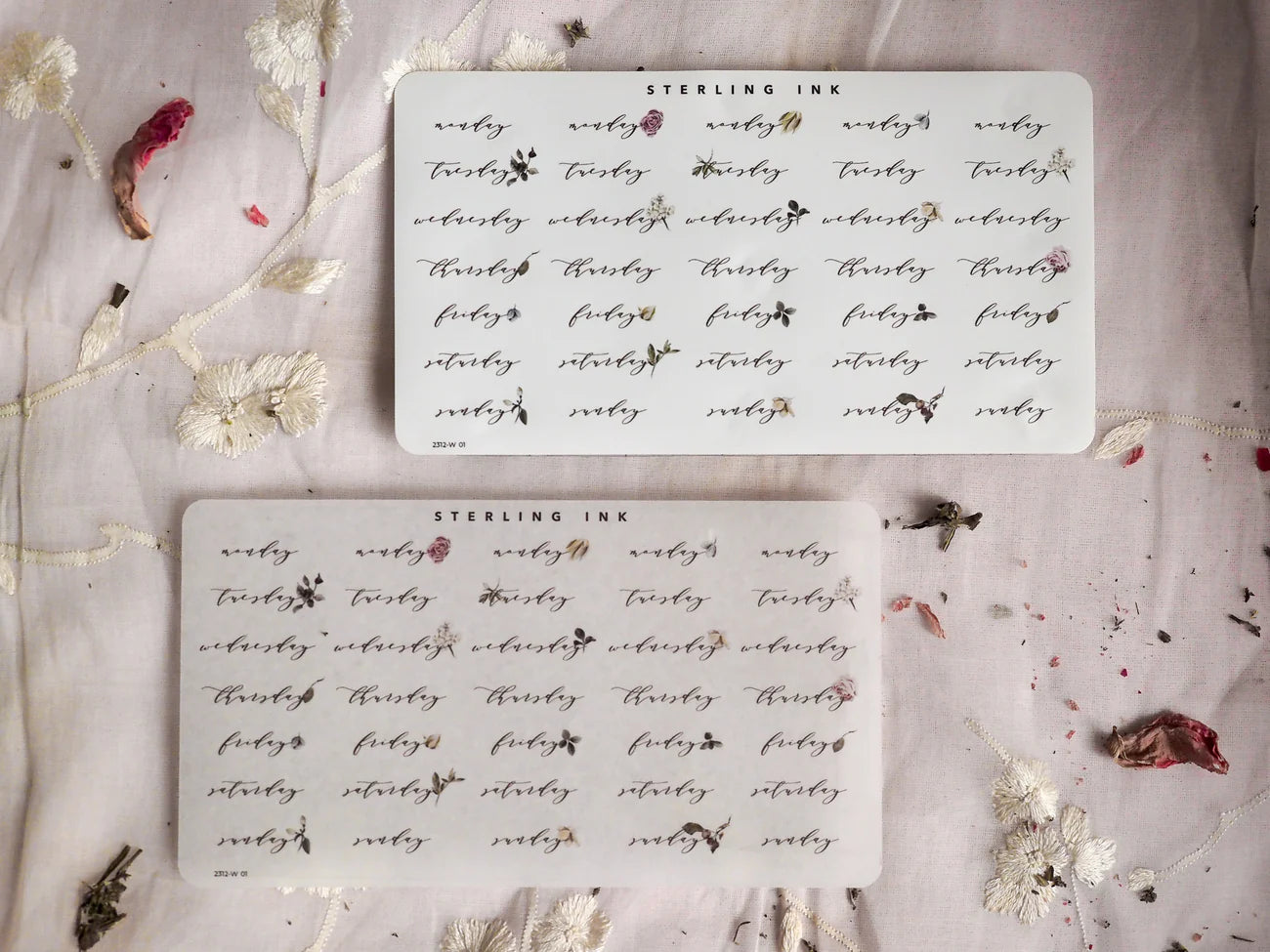 Three sheets of white planner stickers featuring decorative daily labels for weekdays and months, printed with black cursive text and organizational symbols.