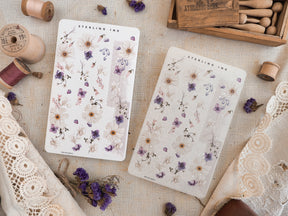 Delicate washi strip stickers featuring a scattered, elegant pattern of white and soft purple spring flowers and foliage, perfect for journaling.