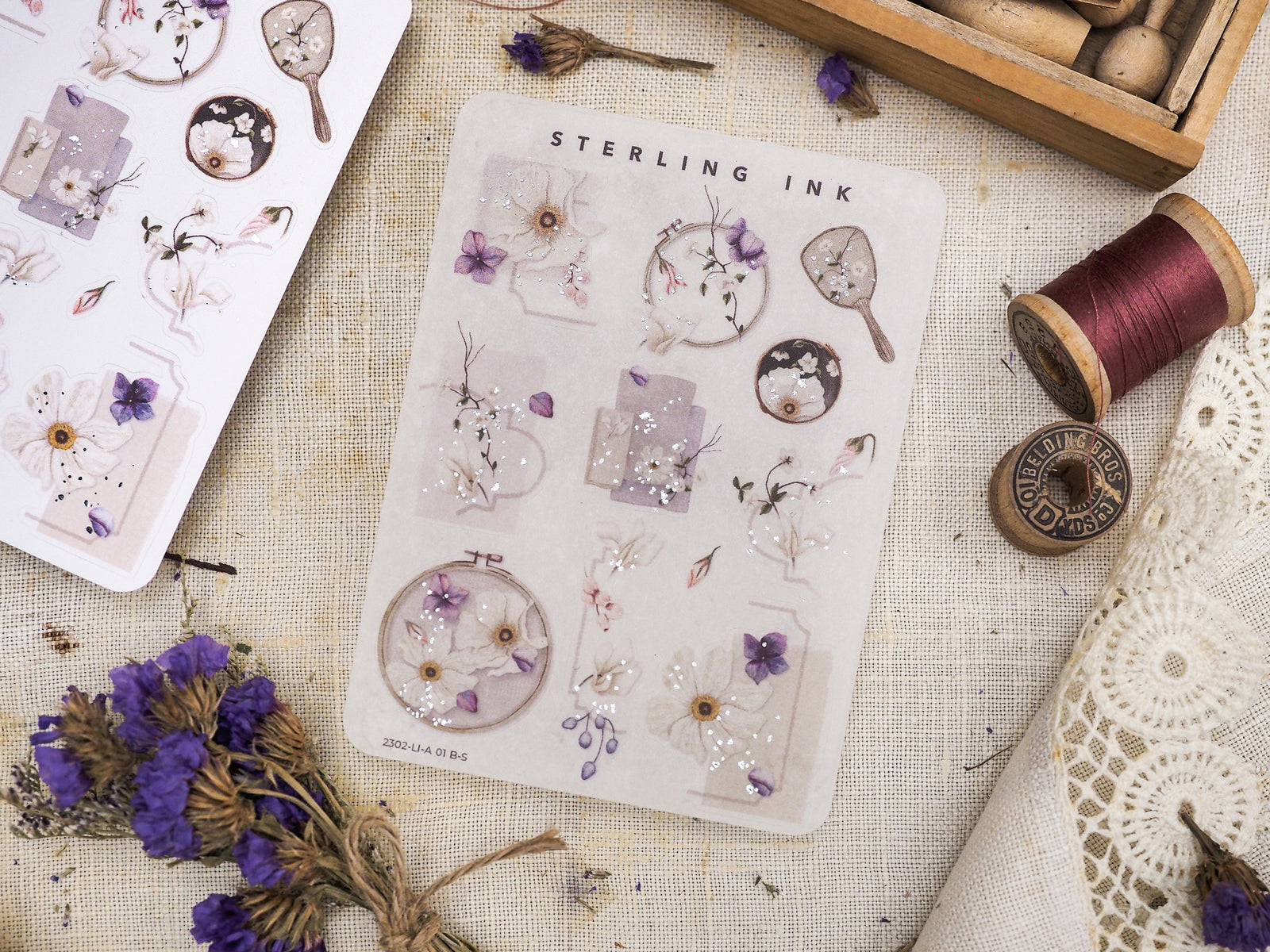 Delicate sticker sheet featuring botanical florals, including pale violets and white blossoms, accented with scattered ink and silver foil details.