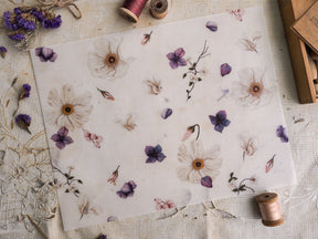 Pale vellum paper featuring a delicate, scattered botanical pattern of cream and muted purple dried flowers and subtle floral sketches.