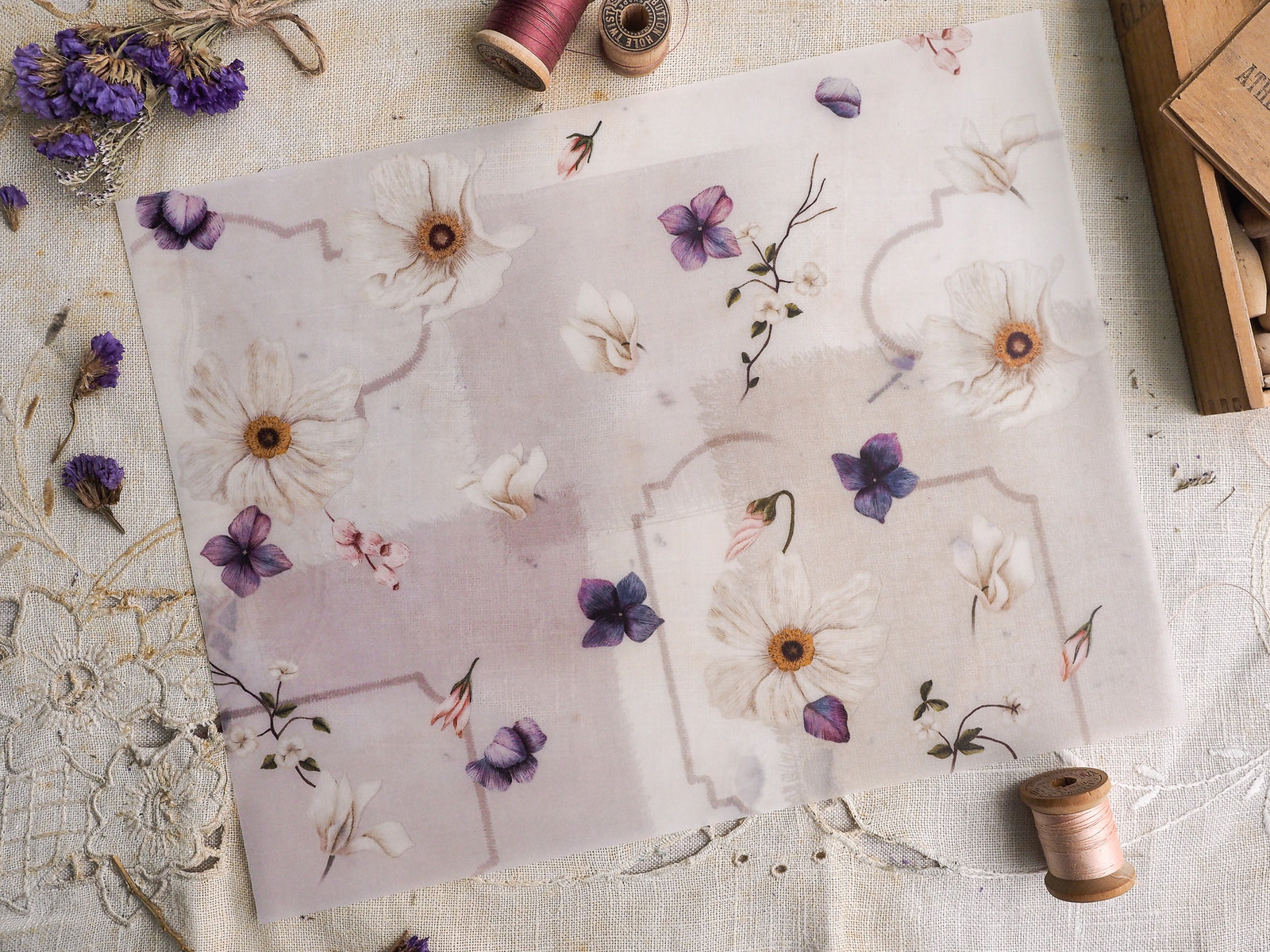 Pale vellum stationery featuring a delicate watercolor botanical pattern of cream and soft purple wildflowers set within subtle geometric borders.