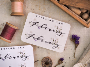 Elegant "Sterling Ink" monthly sticker set for February, featuring delicate script lettering, small butterflies, and watercolor floral accents for journaling and planning.