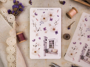 Delicate "Arrangement Stickers - February 2023," featuring watercolor clusters of white and purple flowers and leaves, paired with charming house window illustrations.