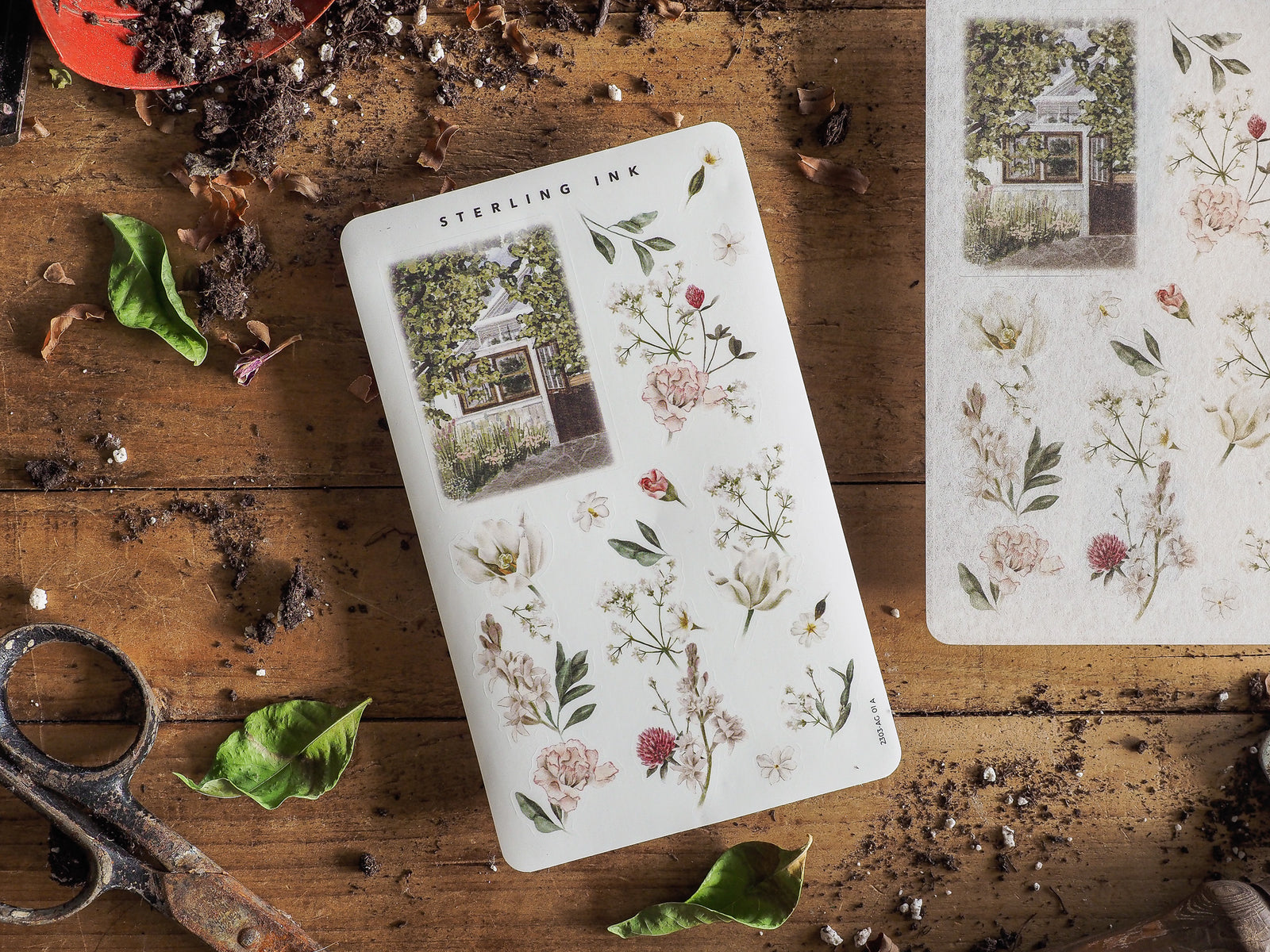 Delicate botanical arrangement sticker sheet featuring lush floral illustrations, varied greenery, and a small vintage photograph of a quaint cottage.