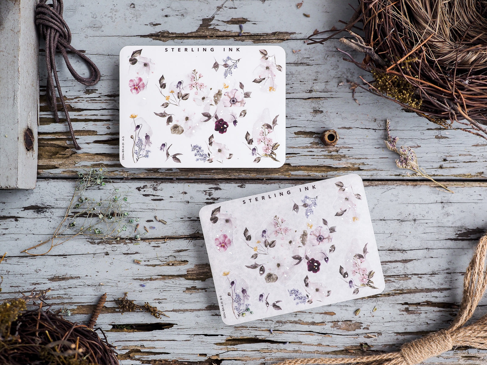 Decorative floral sticker sheets with watercolor clusters of pale mauve and dusty pink flowers, leaves, and botanical elements on a cream background.