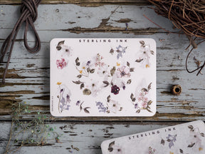Delicate sticker sheet featuring a botanical arrangement of soft watercolor florals, including dusty purples, creams, and muted pink blossoms.