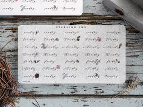 Delicate weekly sticker set featuring dates and weekdays (Monday through Sunday) decorated with small, scattered watercolor florals on cream paper.
