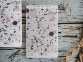 Pale, floral-patterned stickers featuring muted bouquets of blush pink, lavender, and dusty purple blooms arranged on delicate leaves.