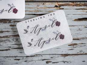 Rustic month sticker for April featuring delicate purple floral accents and the name 'April' in elegant, handwritten script.