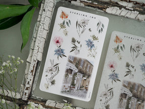 Sticker sheet featuring botanical watercolors of pink and blue flowers alongside a rustic photo of a European building, perfect for crafting May 2023 arrangements.